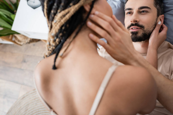 vysoký úhel pohledu na vousatý muž při pohledu na sexy africký Američan žena na rozmazané popředí doma - Fotografie, Obrázek