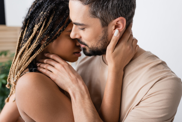 Бічні види брюнетки бородатий чоловік і гаряча афріканська жінка з дредами цілуються вдома - Фото, зображення