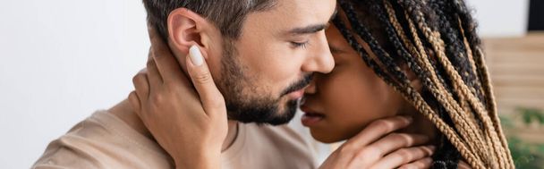 πλαϊνή άποψη του γενειοφόρου άνδρα και νεαρή Αφροαμερικανή γυναίκα με dreadlocks φιλιά στο σπίτι, πανό - Φωτογραφία, εικόνα