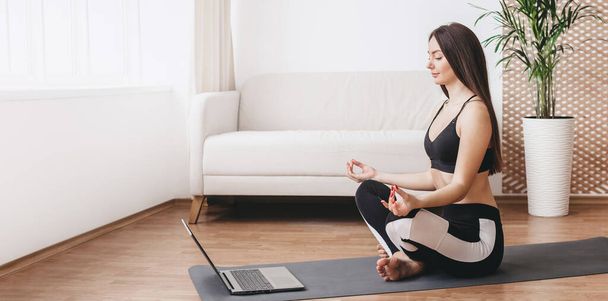 Hermosa mujer haciendo yoga en casa y viendo lección de tutorial en el portátil en un día soleado. Niña aprendiendo a meditar en casa, practicando la respiración. banner web, espacio de copia - Foto, imagen