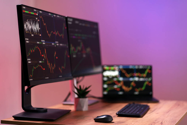 Laptop and computer monitors with crypto charts on the desk, selective focus. Trader workplace concept - Photo, Image