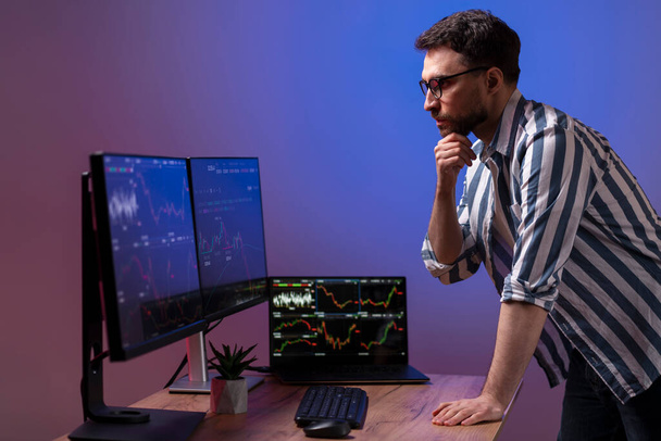 Pewny siebie przystojny poważny handlowiec patrząc na monitor komputera, pracuje online z wykresem crypto w nowoczesnym biurze. Handel online, udana koncepcja biznesowa - Zdjęcie, obraz