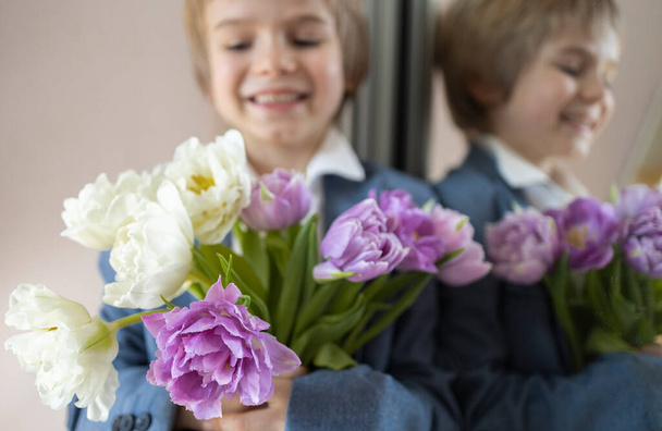 piękny bukiet białych i liliowych tulipanów na pierwszym planie, twarz słodkiego uśmiechniętego chłopca w pobliżu lustra w rozproszeniu. Dzień matki, Walentynki, Urodziny. Uroczysty nastrój, przyjemny kwiat niespodzianka - Zdjęcie, obraz