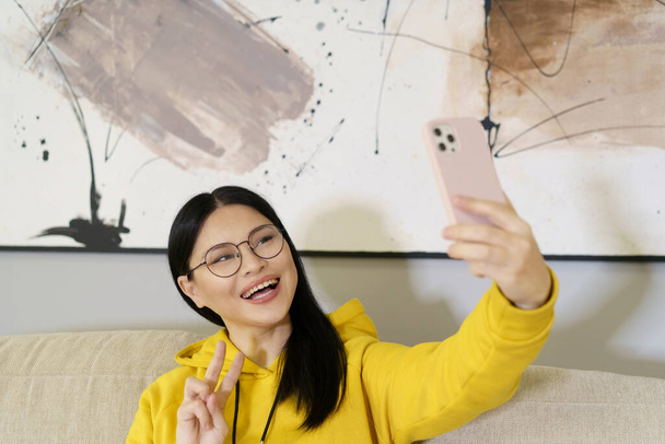 Asian student takes selfie with smartphone, utilizing the latest in mobile photography and communication technology. With glasses on, she captures self-portrait to share on social media or with - Fotografie, Obrázek