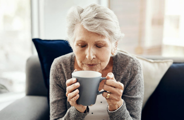 Koffie is de enige vriend die me nooit verlaat. een oudere vrouw genieten van een kopje koffie terwijl ontspannen thuis - Foto, afbeelding
