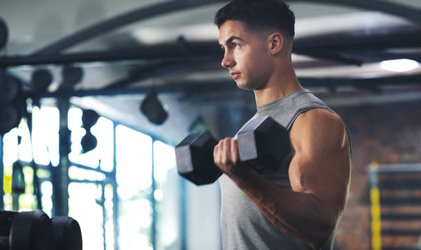 The hardest part about working out should be your muscles. a sporty young man exercising with a dumbbell at the gym - Foto, immagini