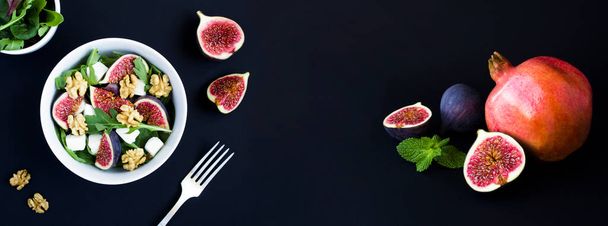 Salade met arugula, feta kaas, vijgen en walnoten in de witte kom op de zwarte achtergrond. Bovenaanzicht. Close-up. - Foto, afbeelding