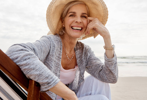 Je ne peux pas rester loin de la plage. Portrait recadré d'une jolie femme d'âge moyen assise sur une chaise longue à la plage - Photo, image