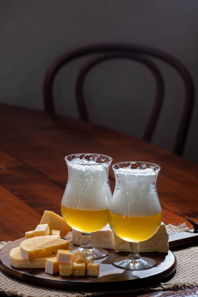 Glasses of Belgian light blonde beer made in abbey and wooden board with variety of belgian cheeses, food and beer pairing - Photo, Image