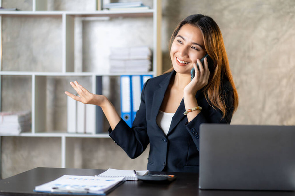 Poważny azjatycki bizneswoman za pomocą telefonu obsługi klienta siedzi przy stole, kierownik sprzedaży koncentruje się kobieta na telefon komórkowy omawianie pracy z klientem w biurze - Zdjęcie, obraz