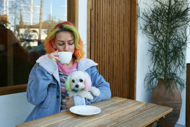 Young woman enjoying the morning cup of coffee with her maltese dog in a pet carrier backpack. Close up, copy space, background. - Foto, Bild