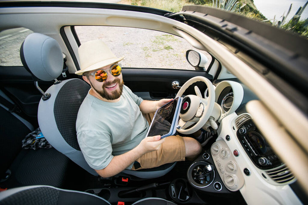 Bearded man using digital tablet inside car while travel and road trip vacation holidays - road map and navigation - Photo, Image