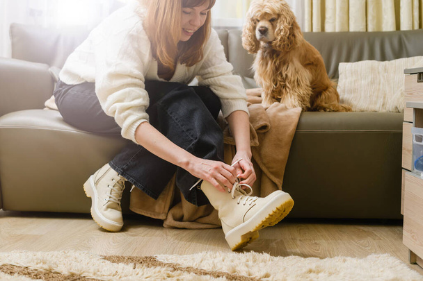 Dziewczyna wiąże sznurowadła przed wyprowadzeniem psa. Pies czeka na kanapie.. - Zdjęcie, obraz