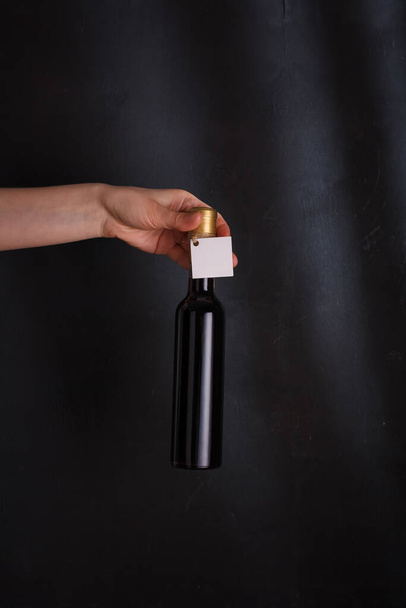manos sosteniendo 250 ml botella de vino tinto con etiqueta simulada, sin marca sobre fondo negro. Cabernet sauvignon, merlot, pinot noir. Bebida alcohólica, espacio para copias - Foto, imagen