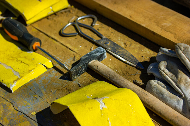Working hand tools lying on a table top view of the rule of diagonals. Hammer, yellow sandpaper, scissors, protective gloves to work in a home garden, on a construction site. Workshop scene flatly. - Photo, Image