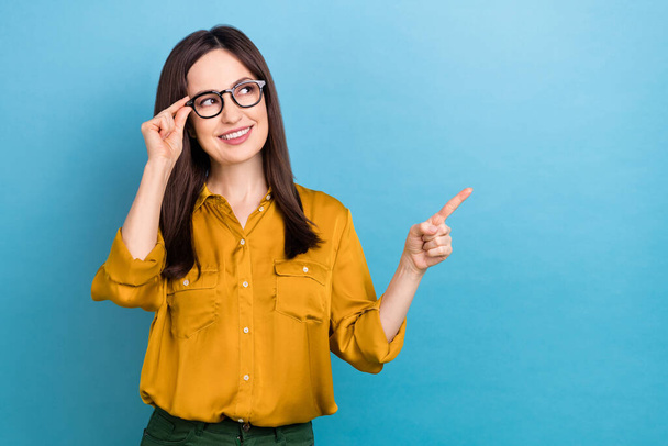 Photo of pretty thoughtful woman wear yellow shirt arm spectacles pointing empty space isolated blue color background. - Fotografie, Obrázek