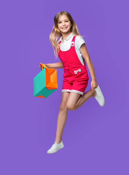 teen girl jumping after shopping on background. photo of teen girl jumping after shopping. teen girl jumping after shopping isolated on purple. teen girl jumping after shopping in studio. - Photo, image