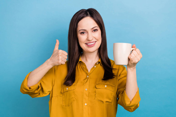 Photo of adorable confident lady dressed yellow shirt showing thumb up drinking tea isolated blue color background. - Φωτογραφία, εικόνα