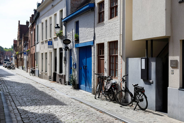 Brugia, Belgia - 12 września 2022 r.: Na wąskiej ulicy obok siebie znajdują się murowane domy. Ich kolorowe okiennice, drzwi i ramy okienne tworzą malowniczy krajobraz miasta. - Zdjęcie, obraz