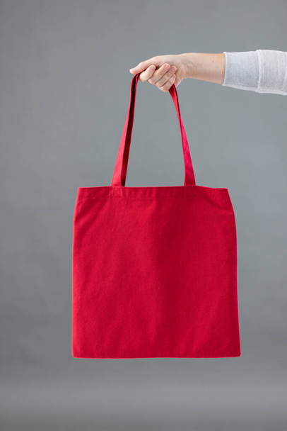 Hand of caucasian woman holding red canvas bag with copy space on grey background. Bags and fashion concept. - Fotoğraf, Görsel