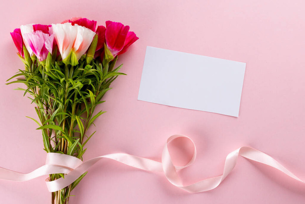 Image of pink and white flowers with ribbon and card with copy space on pink background. Mothers day, nature and spring concept. - 写真・画像