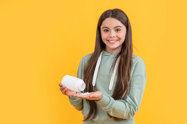 positive teen girl with medication isolated on yellow. teen girl with medication in studio. teen girl with medication on background. photo of teen girl with medication pill. - Фото, зображення