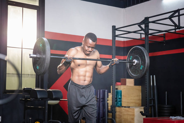 Afrikalı Amerikalı fitness adamı spor salonunda ağırlık kaldırıyor, kaslı adam spor salonunda halter ağırlığıyla egzersiz yapıyor. - Fotoğraf, Görsel