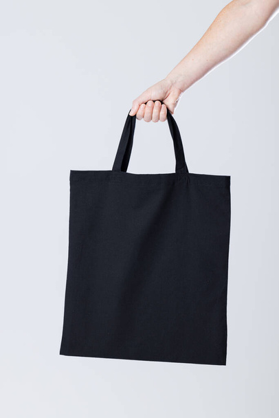 Hand of caucasian woman holding black canvas bag with copy space on grey background. Bags and fashion concept. - Foto, immagini