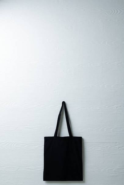 Hanging black canvas bag on white wall background with copy space. Eco friendly shopping bags and fashion concept. - Φωτογραφία, εικόνα