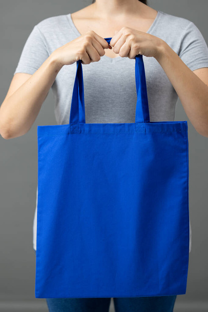 Caucasian woman holding blue canvas bag with copy space on grey background. Bags and fashion concept. - Φωτογραφία, εικόνα