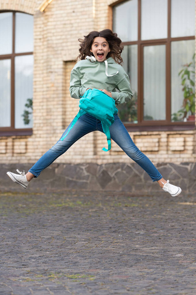 photo of surprised school girl jump childhood with backpack. school girl childhood jump outdoor. school girl jump childhood outside. school girl jump childhood at the street. - Фото, зображення