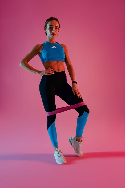 Спортивная женщина тренирует ноги с фитнес-эластичной лентой на студийном фоне. Высокое качество фото - Фото, изображение