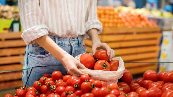 Kobieta zbierająca pomidory w torbie wielokrotnego użytku w sklepie. Ekologia i matematyka Dnia Ziemi - Zdjęcie, obraz