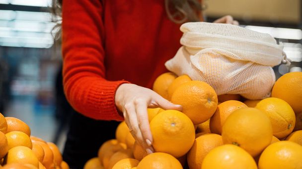 Kobieta zbierająca pomarańcze w torbie wielokrotnego użytku w sklepie. Ekologia i matematyka Dnia Ziemi - Zdjęcie, obraz