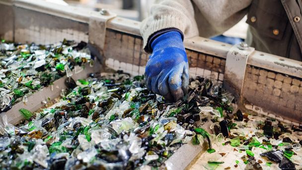 Worker in special gloves sorting glass garbage on a vibrating conveyor belt at waste sorting plant - Foto, Imagem