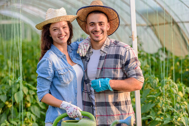 happy young couple with watering can in greenhouse. - Photo, Image