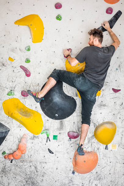 Jonge klimmer klimmend op een rotswand binnen, achteraanzicht, concept van extreme sporten en boulderen - Foto, afbeelding