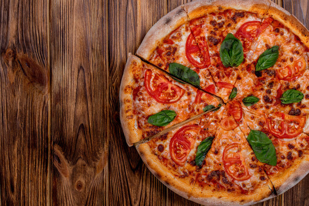 Delicious fragrant pizza-Margherita with mozzarella, tomatoes and basil on tomato sauce on woden background. Copy space. - Photo, Image