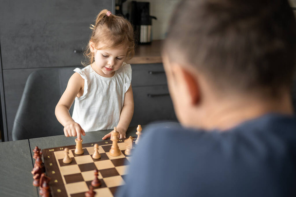 Der Vater bringt seiner kleinen Tochter das Schachspielen am Tisch in der heimischen Küche bei. Das Konzept der frühkindlichen Entwicklung und Bildung. Familienfreizeit, Kommunikation und Erholung. Hochwertiges Foto - Foto, Bild