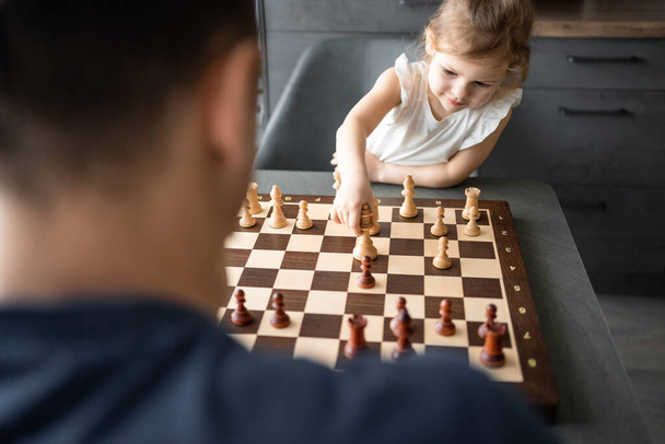Father teaching his little daughter to play chess at the table in home kitchen. The concept early childhood development and education. Family leisure, communication and recreation. High quality photo - Foto, afbeelding