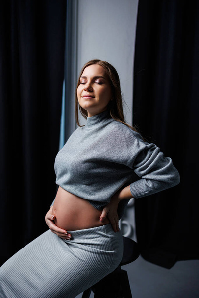 Aranyos terhes nő pulóverben és szoknyában, pocakkal. Boldog, elegáns terhes nő. Egy nő gyermeket vár. - Fotó, kép