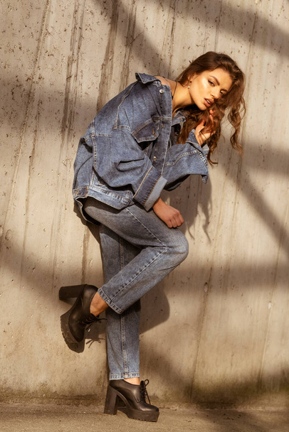 Attractive Latino woman in denim jacket and jeans on grey wall background. - Photo, Image