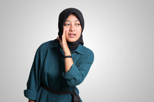Portret wesołej Azjatki z hidżabem, próbującej usłyszeć plotki lub dźwięk, trzymającej się za rękę blisko ucha i słuchającej uważnie. Koncepcja reklamy. Izolowany obraz na białym tle - Zdjęcie, obraz