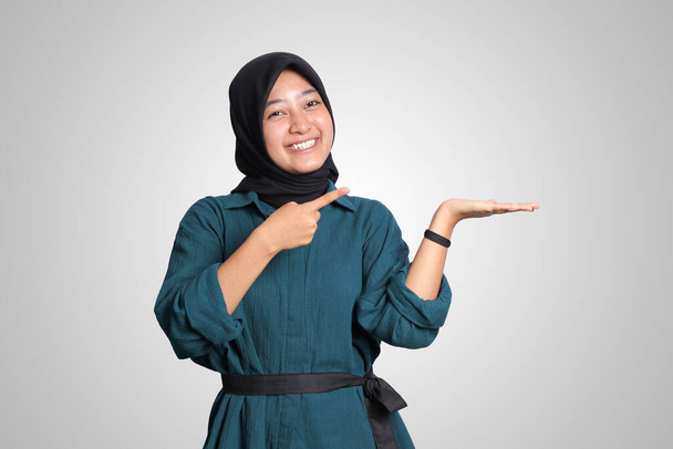 Portré izgatott ázsiai hidzsáb nő alkalmi ruhát áll szemben a fehér háttér, mutatja a termék és a mutató kézzel és ujjal oldalra. Hirdetési koncepció. - Fotó, kép