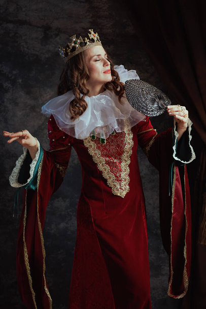medieval queen in red dress with fan, white collar and crown on dark gray background. - Фото, зображення