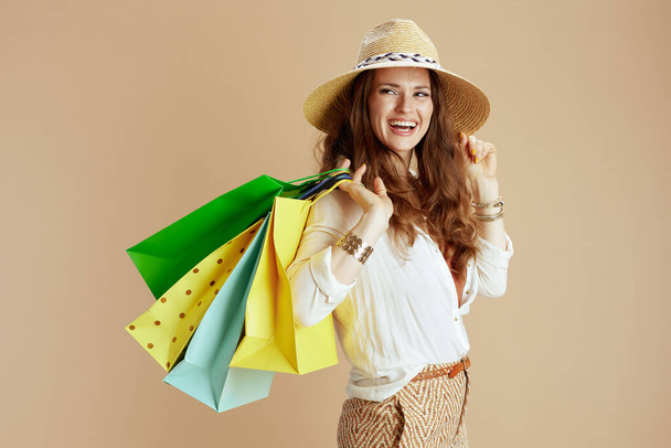 Beach vacation. happy modern middle aged housewife in white blouse and shorts isolated on beige with shopping bag and straw hat. - Фото, зображення