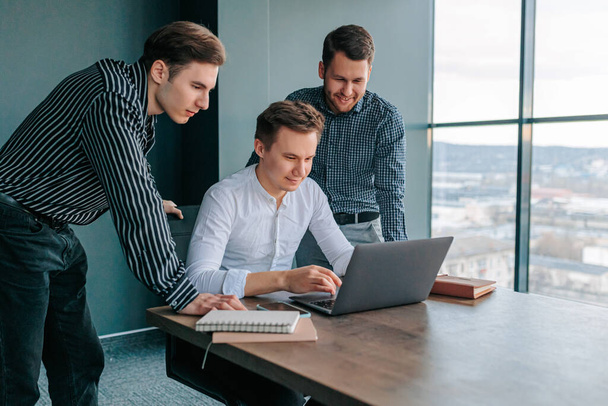 Three young men sitting in an office, working on their laptops and collaborating on a project. group of people in business attire, including a businessman and his two colleagues, all typing away - Foto, Bild