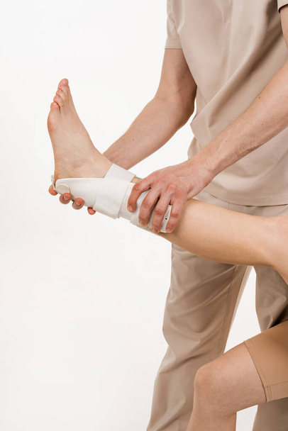 Travmatolog, yaralanmaları atlatmak ve yeni yaralanma riskini azaltmak için bacağa dış bilek ya da ayak bandajı takıyor. Ayak bileği ve ayak bileği eklemlerinin patolojik hareketini azaltmak için dış ortozu. - Fotoğraf, Görsel