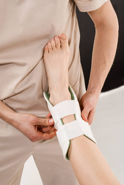 Ayak bileği ve ayak dış ortozu ayak bileklerindeki patolojik hareketliliği azaltmak için. Travmatolog, yaraları iyileştirmek ve yeni yaralanma riskini azaltmak için bacağa dış bilek ya da ayak bandajı takıyor. - Fotoğraf, Görsel