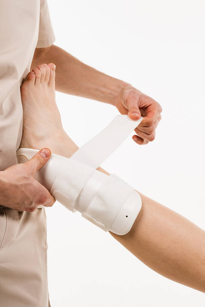 Traumatologist puts external ankle or foot bandage on leg to recover from injuries and reduce risk of new injuries. Ankle and foot external orthosis to reduce pathological mobility of ankle joints - Fotó, kép